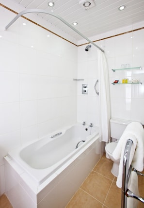 Un baño moderno con una bañera grande, ducha e inodoro. Hay repisas con artículos de aseo personal y un perchero.
