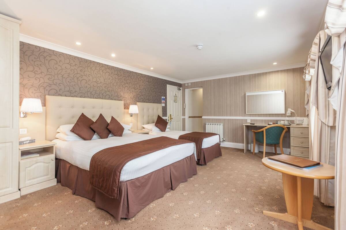 Une chambre d’hôtel avec deux lits, un bureau, une chaise, une télévision et une armoire.