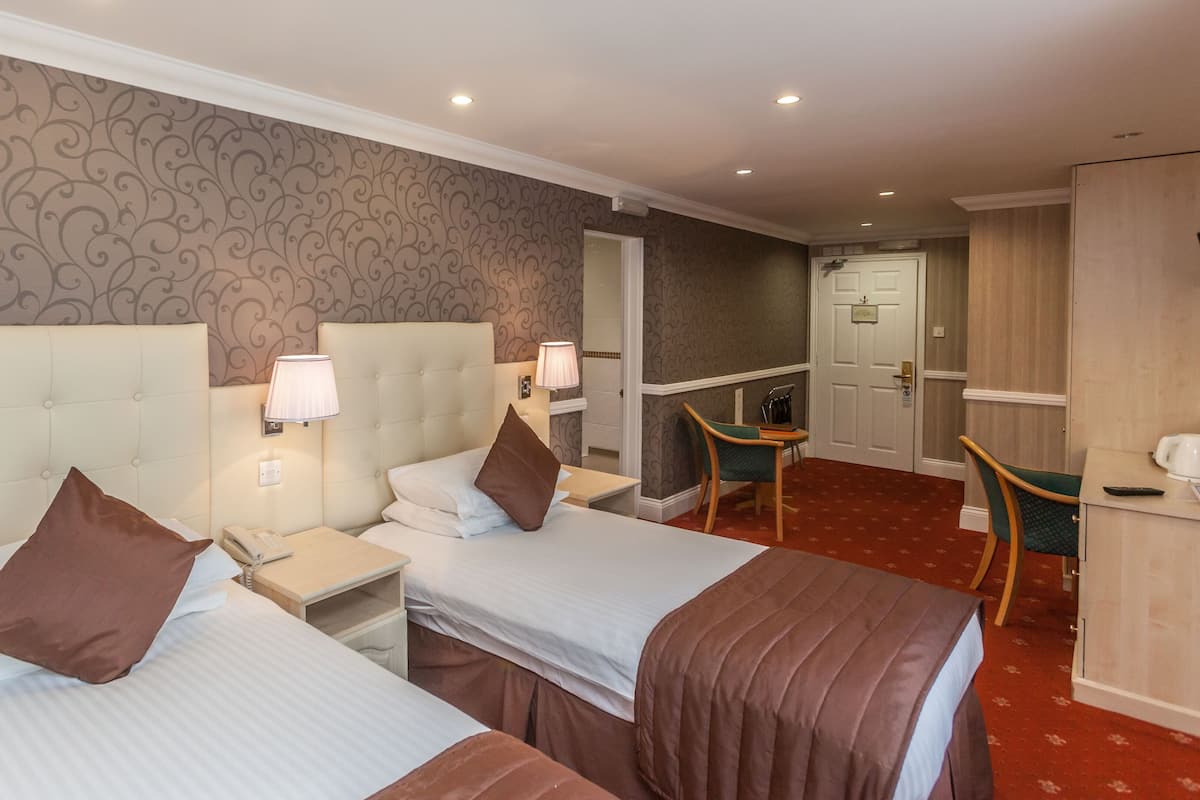 Une chambre d’hôtel avec deux lits, un bureau, une chaise, une lampe et une porte donnant sur une salle de bain.