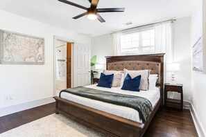 A bedroom with a wooden bed, a ceiling fan, a window with curtains, and a map on the wall.