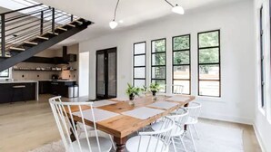 A spacious dining area with a wooden table and white chairs, large windows, and a staircase leading to an upper level. - Sleek & Beautiful New Luxury Home In Atlanta (Atlanta)