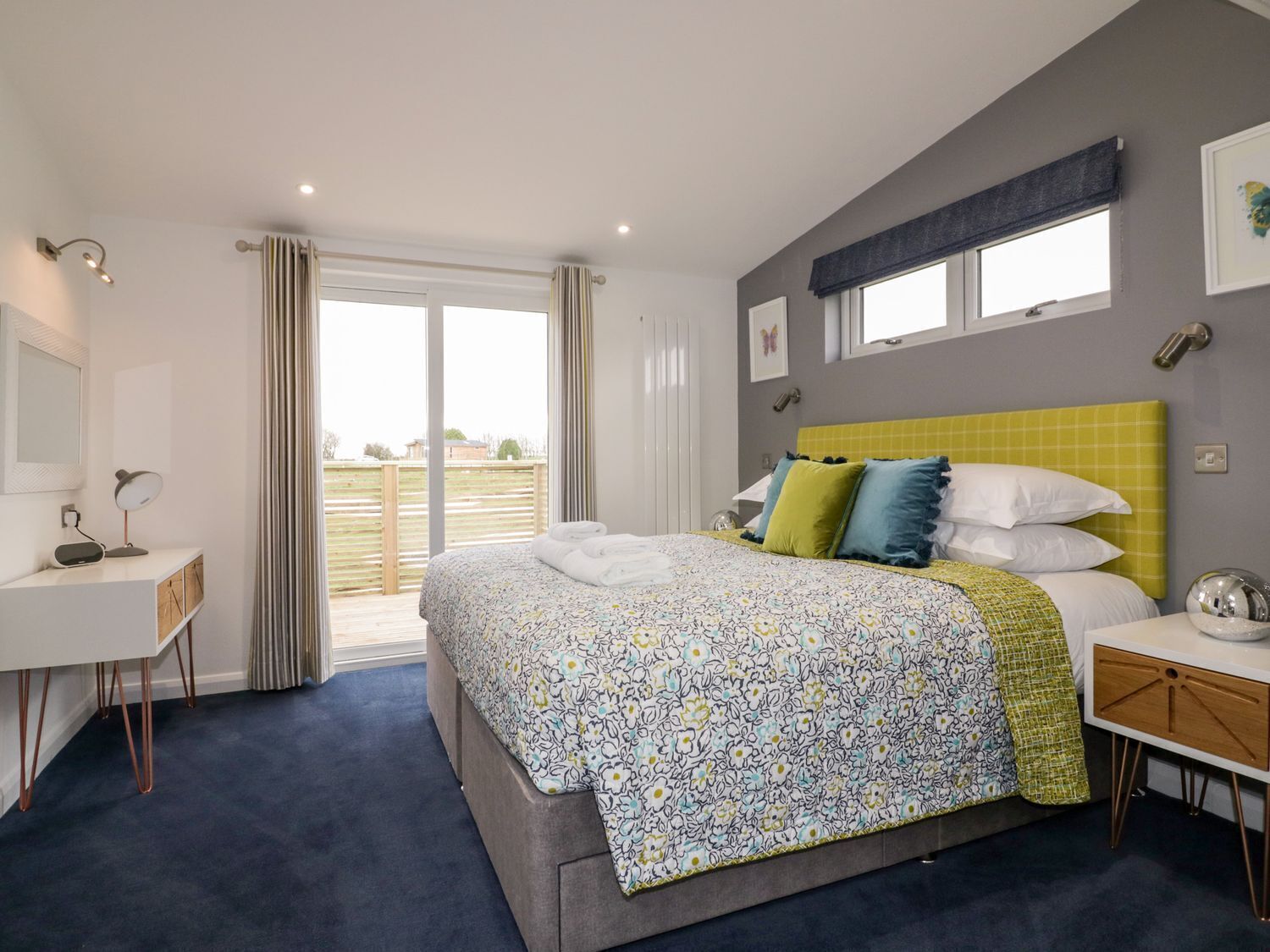 A bedroom with a bed, bedside table, and a desk with a lamp.