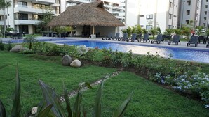 A hotel pool area with a thatched-roof structure, lounge chairs, and a well-maintained lawn. - CONDO LOMA by TRVL2HM (Nuevo Nayarit)
