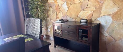 A corner of a room with a stone wall, a dark wooden cabinet with glass doors, and a wicker basket with a plant.