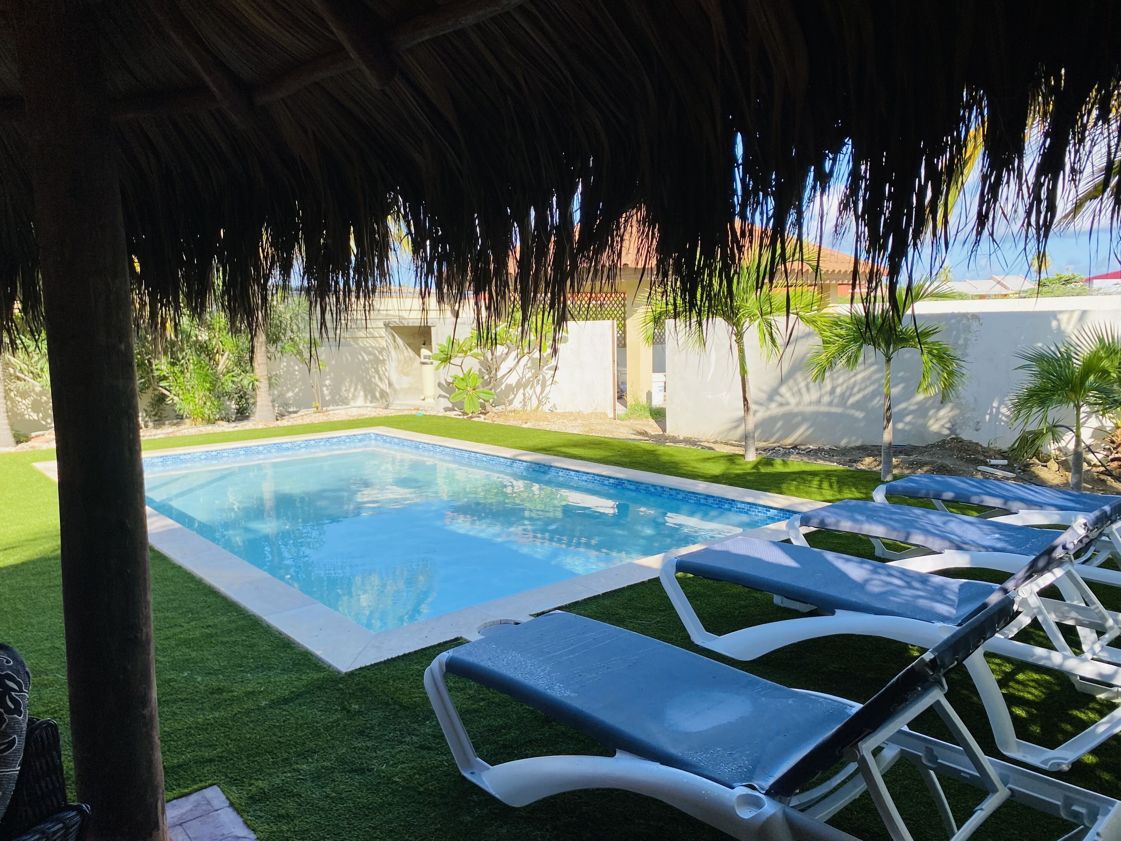 Una piscina con agua azul cristalina, rodeada de césped artificial y sillas reclinables blancas.