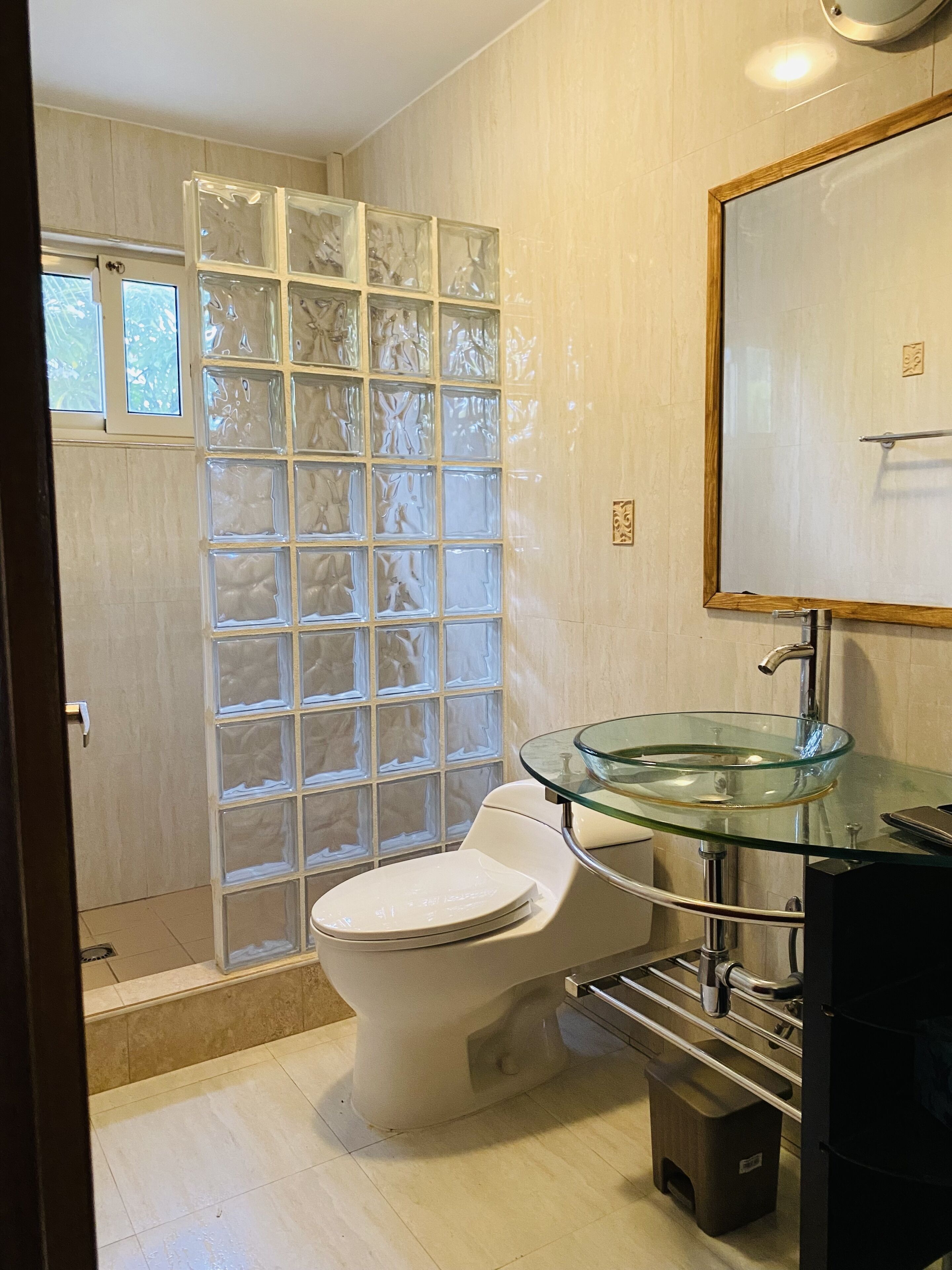 Un baño con lavamanos de vidrio, inodoro y cabina de ducha con paneles de vidrio satinado.