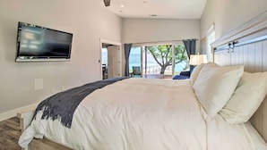 Un dormitorio con una cama grande, un ventilador de techo, un televisor montado en la pared y vistas al exterior a través de una puerta.