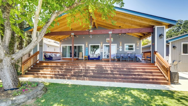 Un espacio exterior techado con piso de madera, una mesa y sillas integradas, y una escalera que conduce a un acceso cubierto.
