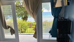 A bedroom with a bed, a blue rug, a TV on the wall, and a balcony with a view of the sea. - Sea Breeze Studio At Carib Resort (Ocho Rios)