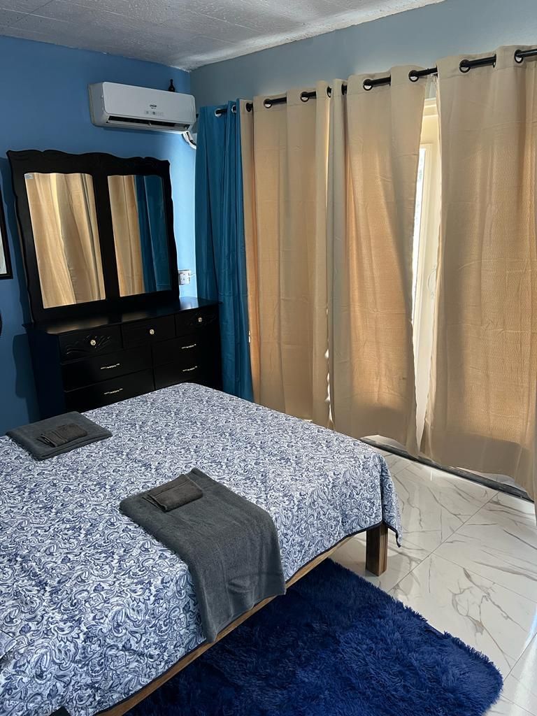 A bedroom with a bed, a dresser, a mirror, and curtains.