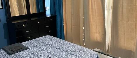 A bedroom with a bed, a dresser, a mirror, and curtains.