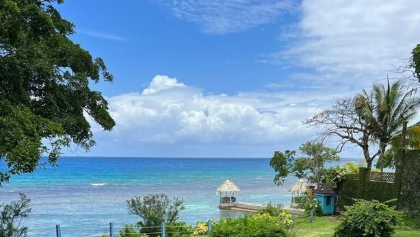 A well-maintained lawn with a small gazebo and a thatched-roof hut by the ocean. - Sea Breeze Studio At Carib Resort (Ocho Rios)
