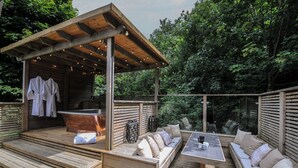 Eine Holzterrasse mit überdachter Sitzgelegenheit, einem Whirlpool und einem Tisch mit Stühlen.