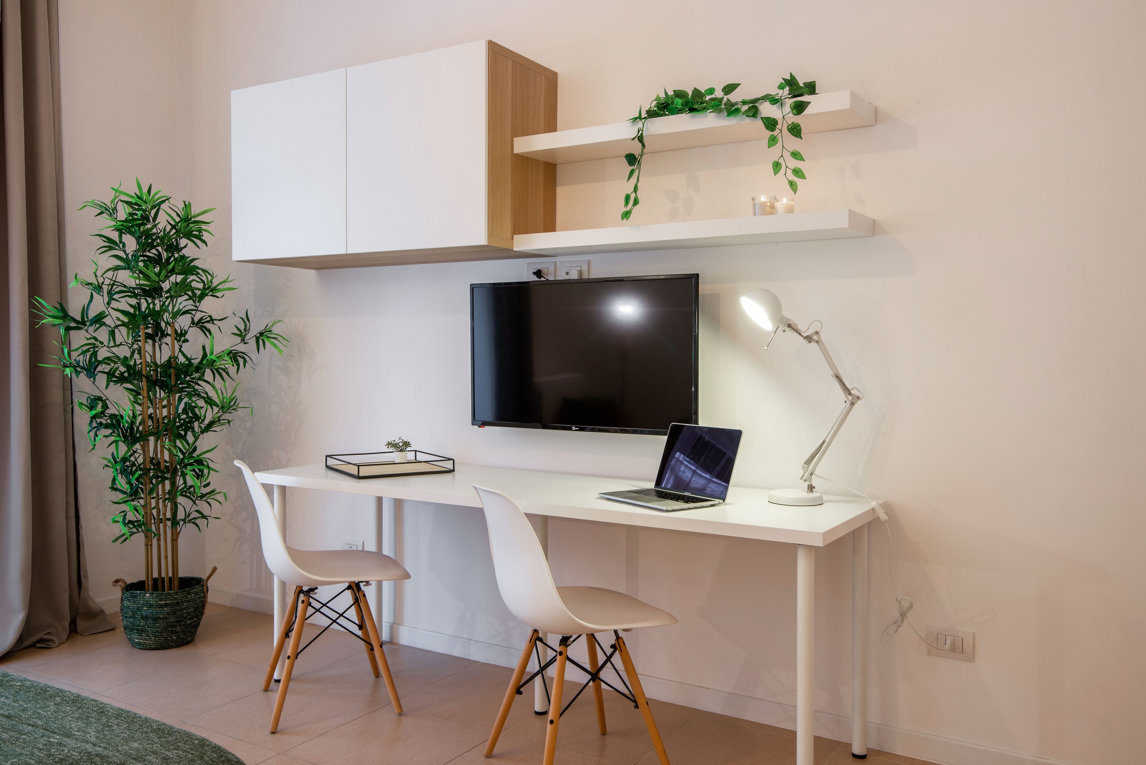 Een moderne werkruimte met een bureau, twee stoelen, een laptop, een televisie en een potplant.
