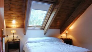 A bedroom with a sloped ceiling, a skylight, a bed, two bedside tables with lamps, and a wooden floor.