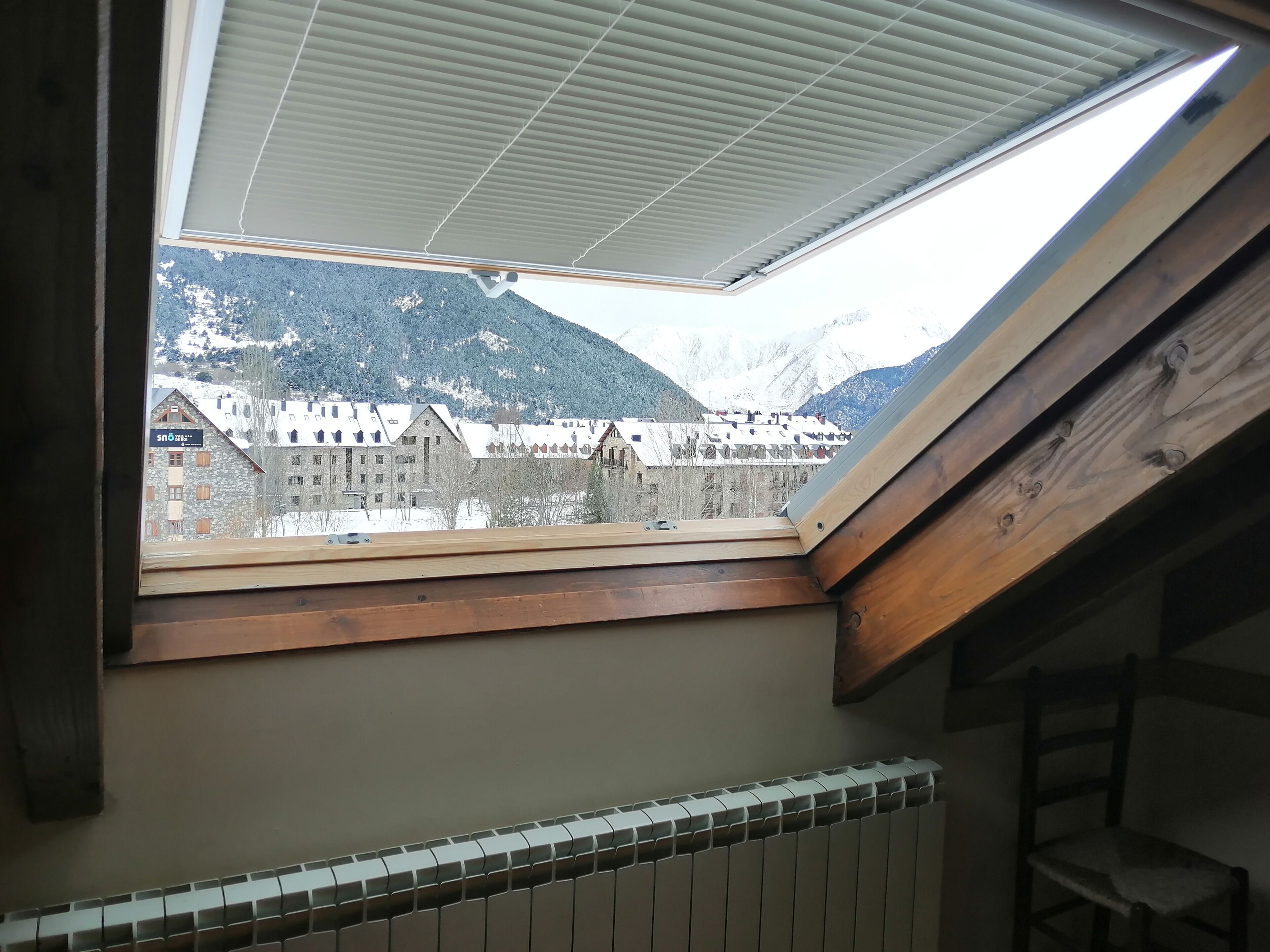 Een dakvenster met uitzicht op besneeuwde bergen en gebouwen.