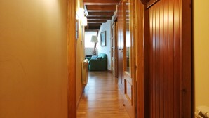 A wooden hallway with a door leading to a room with a bed and a lamp.