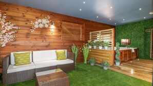 A cozy room with a wooden wall, a white sofa with green cushions, a small table, and a green artificial grass floor. - 9 Meadow Retreat (Liskeard)