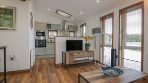 A modern kitchen with a built-in oven, microwave, and a large window with blinds. - 9 Meadow Retreat (Liskeard)