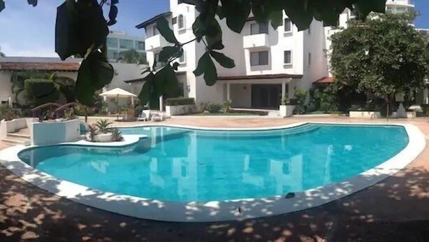 A swimming pool with a curved edge, surrounded by a paved area and potted plants. - Condo Alamandra by TRVL2HM (Nuevo Nayarit)