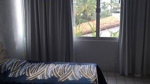 A hotel room with a bed, curtains, and a window with a view of palm trees and buildings. - Condo Alamandra by TRVL2HM (Nuevo Nayarit)