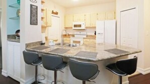 Une cuisine moderne dotée d’un îlot central, de tabourets de bar et de meubles blancs.