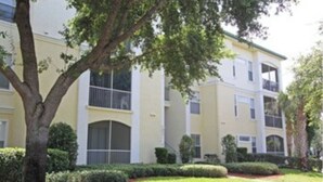 Un immeuble à plusieurs étages doté de balcons, entouré de pelouses et d’arbres bien entretenus.