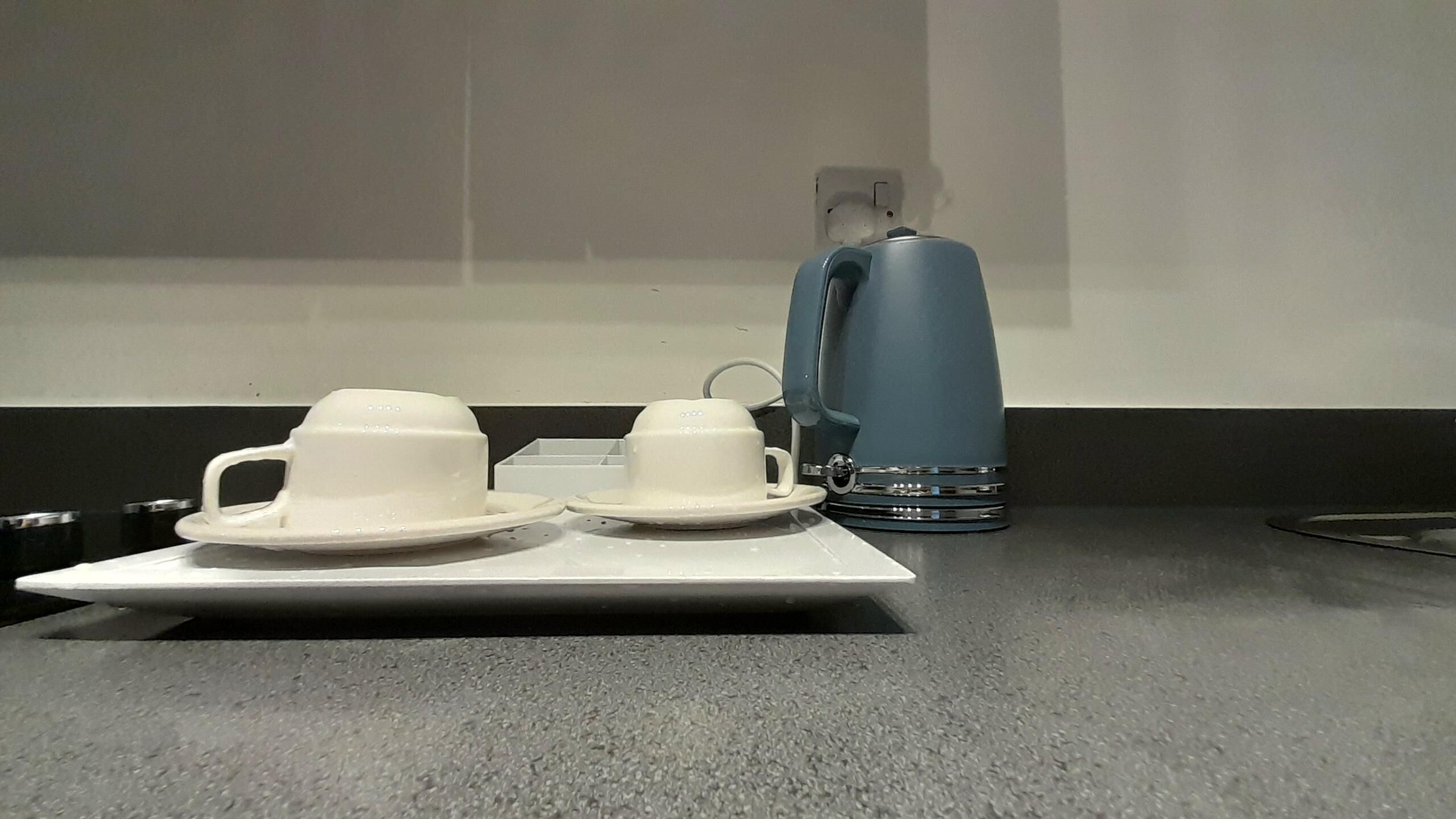 Un coin café avec deux tasses blanches et une machine à café bleue, le tout posé sur un comptoir.