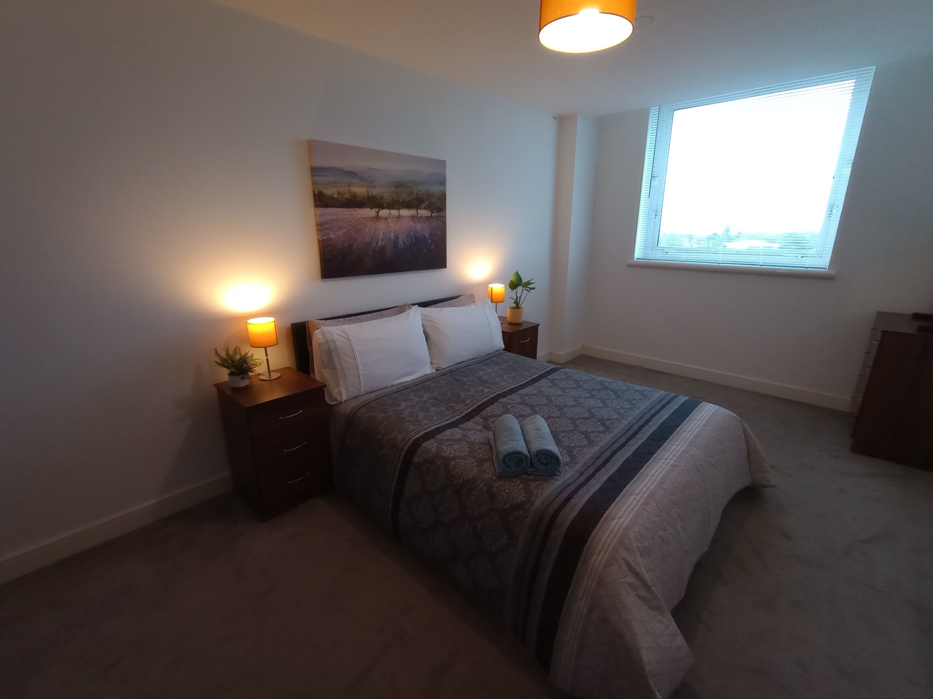 Une chambre à coucher avec un lit, des lampes de chevet, une fenêtre et un tableau au mur.