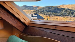 Une pièce dotée d’une lucarne, d’un banc en bois et offrant une vue sur un paysage montagneux.