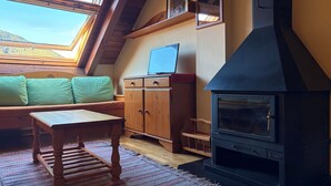 Une pièce chaleureuse avec un banc en bois, une petite table, un téléviseur posé sur un meuble et un poêle à bois.