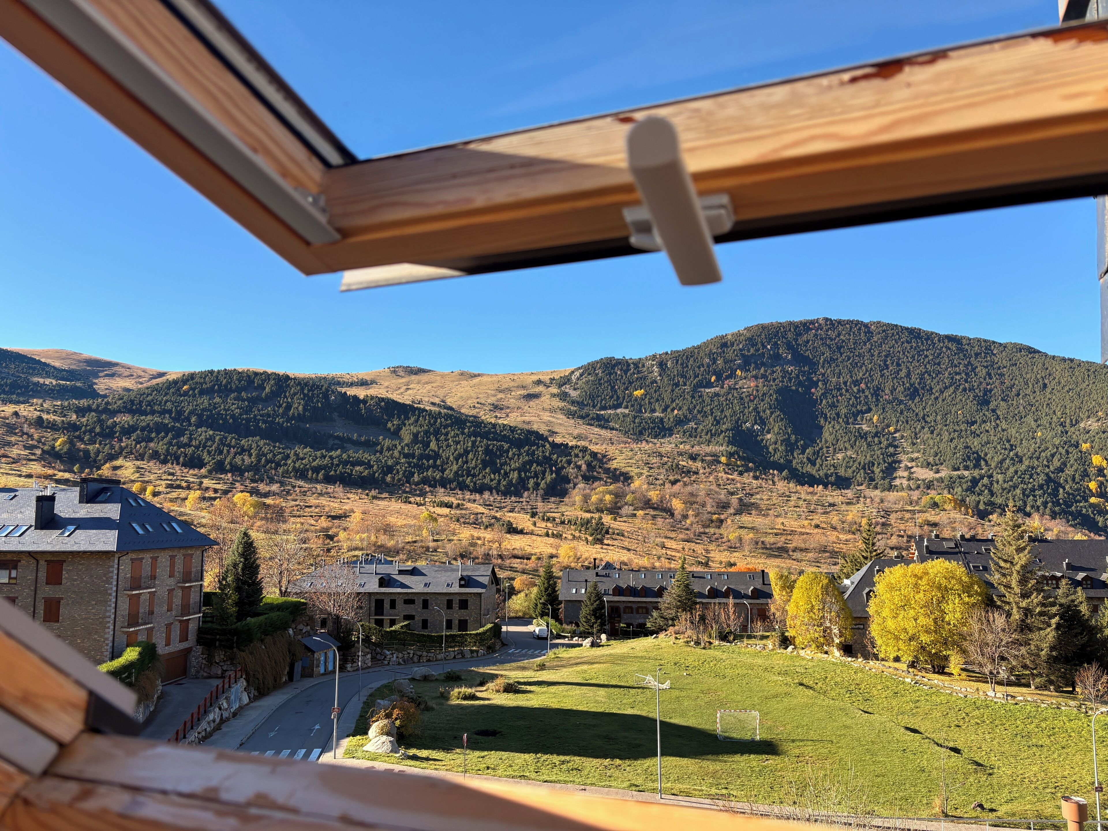 A view from a window overlooking a residential area with houses, a grassy field, and a mountain in the background.