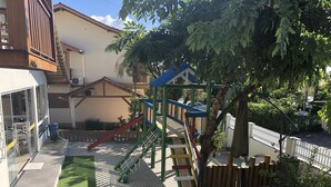 A playground with slides and climbing structures, surrounded by a wooden fence and greenery. - Pousada Rosália (Penha)