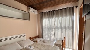 A hotel room with a wooden ceiling, a large bed with a floral quilt, two bedside tables, a mirror, and a window with curtains. - Pousada Rosália (Penha)