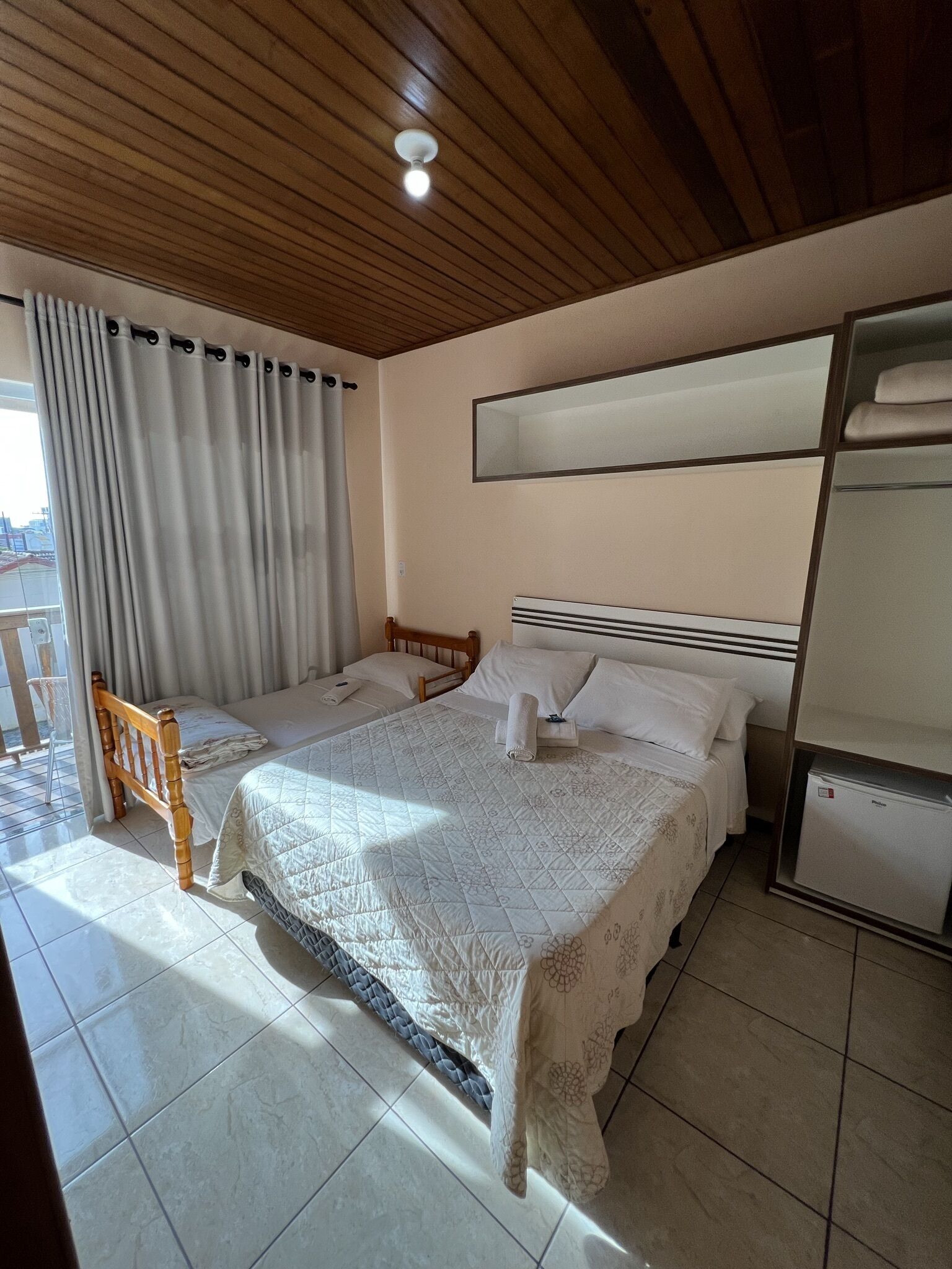 A hotel room with two beds, a wooden ceiling, a large mirror, and a refrigerator.