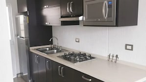 A modern kitchen with dark cabinets, a stainless steel refrigerator, a microwave, and a gas stove.