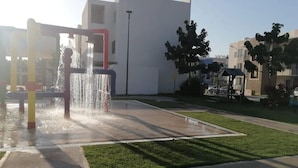A water feature with a fountain in a public square with buildings and trees in the background.