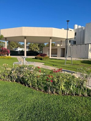 A modern building with a covered outdoor area, a pathway, and landscaped gardens with various plants. - CONDO CARIMA by TRVL2HM (Mezcales)