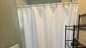 A bathroom with a shower curtain, a toilet, a shelf with towels, and a bathtub.