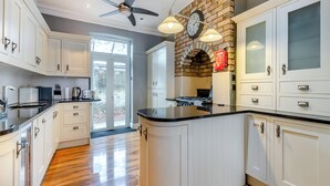 A kitchen with white cabinets, a brick wall, a gas stove, and a ceiling fan.