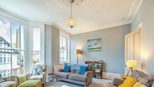 A living room with a sofa, armchairs, a coffee table, a lamp, a bookshelf, and a painting on the wall.