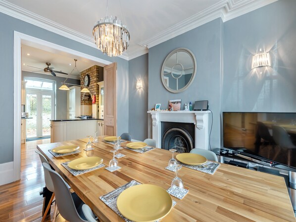 Comedor con mesa de madera dispuesta para seis personas, chimenea y televisor.