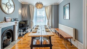 A dining room with a long table, chairs, a fireplace, a television, and a chandelier.