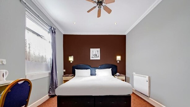 Ein Hotelzimmer mit einem großen Bett, einem Schreibtisch mit Stuhl, einem Deckenventilator und einem Fenster mit Vorhängen.