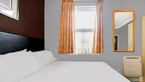 Ein Hotelzimmer mit einem großen Bett, einem Fenster mit Vorhängen, einem Spiegel und einer Heizung.