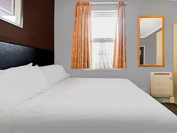 Une chambre d’hôtel avec un grand lit, une fenêtre avec des rideaux, un miroir et un radiateur.