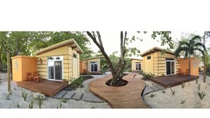 Une rangée de petits bâtiments à un seul étage, dotés de terrasses en bois et d’un arbre au centre.