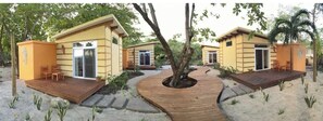 Une rangée de petits bâtiments à un seul étage, dotés de terrasses en bois et d’un arbre au centre.