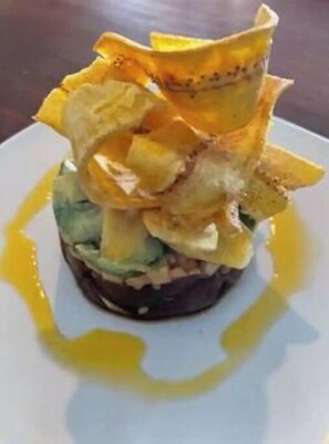 A delicious breakfast dish features a slice of bread topped with avocado and a crispy fried item, served with a side of tangy sauce.