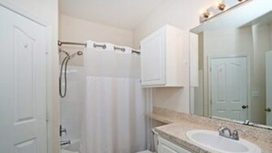 Een badkamer met douche, toilet, wastafel en kastjes.